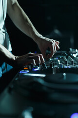 Hands of DJ mixing music on sound mixer on stage. Club disc jockey plays set on party