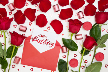 Composition of red roses, chocolates, sequins hearts, envelopes, candles, inscription Happy Birthday. Advertising content for Birthday. Flat lay, top view, close up, copy space on white background