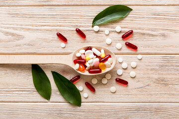 Vitamin capsules in a spoon on a colored background. Pills served as a healthy meal. Red soft gel vitamin supplement capsules on spoon