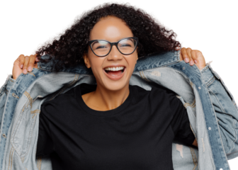 Isolated shot of curly cheerful woman tries on new denim jacket, wears optical glasses, smiles broadly, has perfect mood, poses against pink wall. Positive emotions. Afro female in stylish clothes