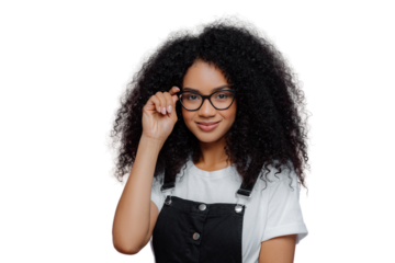 Pretty African American woman keeps hand on frame of glasses, smiles happily, wears white casual t shirt and black overalls, enjoys spare time, poses over violet background. Ethnicity, fashion concept