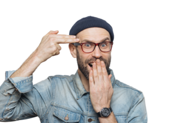 Funny bearded man foolishes indoor, pretends to kiss himself with gun or making suicide gesture, covers mouth with hand, looks joyfully into camera, isolated over grey background. Male foolishes