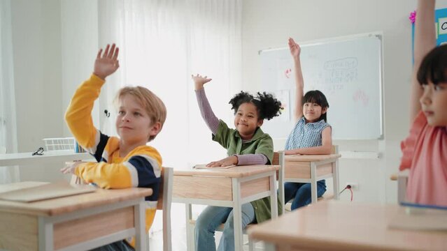 Elementary students raising hands to answer question from teacher in the classroom at school