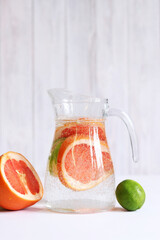 Pitcher with lemonade on a light wooden background. Summer fortified drink. Grapefruit, lime and mineral water lemonade. Jug with drink and fruits nearby