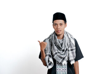 Religious muslim asian man wearing turban, muslim dress and cap, pointing to the side of empty space. Isolated on white background.
