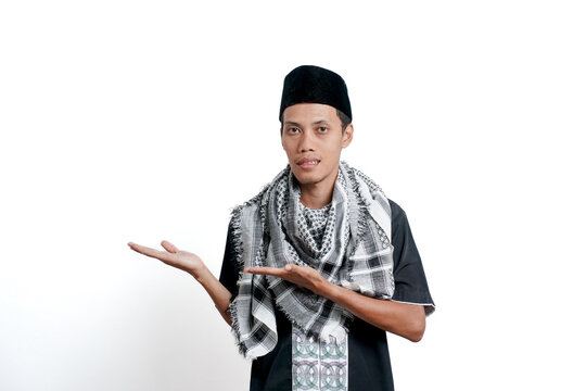 Religious muslim asian man wearing turban, muslim dress and cap, pointing to the side of empty space. Isolated on white background.