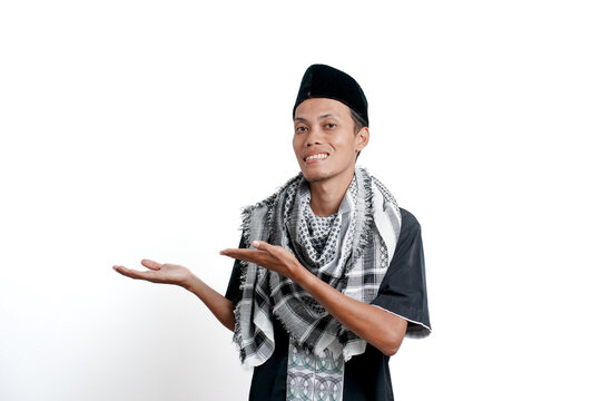 Religious muslim asian man wearing turban, muslim dress and cap, pointing to the side of empty space. Isolated on white background.