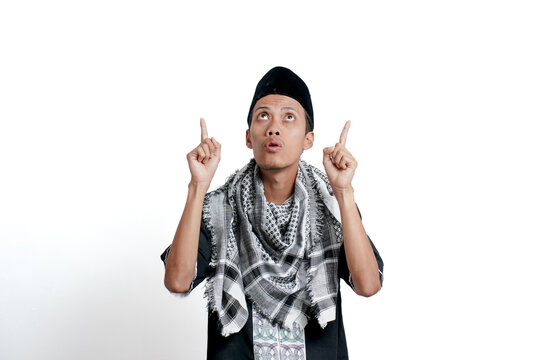 Asian religious Muslim man wearing turban, Muslim dress and cap, pointing up empty space with excited expression. Isolated on white background.