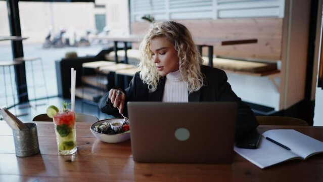 Busy businesswoman does not have time to eat while sitting at table in cafe and is forced to interrupt lunch to answer phone call. Remote work on a computer, how to organize a work schedule