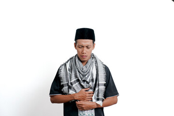 Religious muslim asian man wearing turban, muslim dress and cap, feeling pain due to stomach ache or ulcer. Isolated on white background.