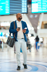 Black man checking flight schedule with phone and ticket walking in airport terminal, holding...