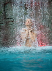 beautiful young cute sexy blonde nude woman enjoying relaxed the splashing water of the waterfall in the Spa Wellness, feels the falling water