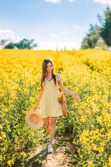 Naklejka na ściany i meble girl in white sneakers and a yellow dress with a hat in her hands in a yellow field