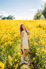 Naklejka na ściany i meble girl walks in a yellow field of rapeseed. A woman with a bouquet of flowers in her bag
