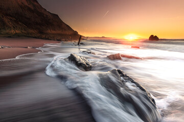 Sunset while sea waves hitting the rocks on the beach; at Ilbarritz beach in Biarritz, Basque...