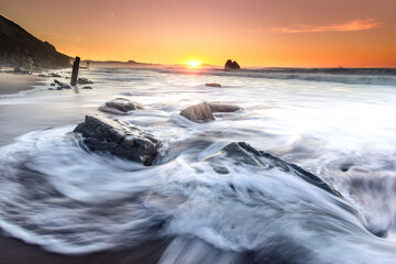 Sunset while sea waves hitting the rocks on the beach; at Ilbarritz beach in Biarritz, Basque Country.