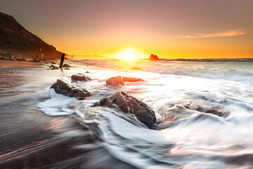 Sunset while sea waves hitting the rocks on the beach; at Ilbarritz beach in Biarritz, Basque Country. - obrazy, fototapety, plakaty