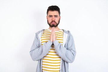 Positive caucasian man wearing casual sportswear over white wall  smiles happily, glad to receive pleasant news from interlocutor, keeps palms together, People emotions concept.