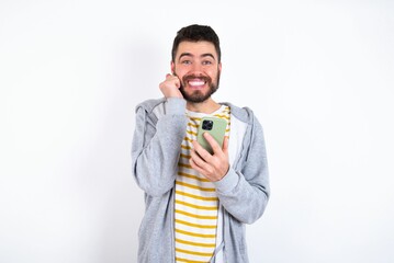 Joyous caucasian man wearing casual sportswear poses with mobile phone device, types text message on modern smartphone, watches funny video during free time, enjoys good internet connection,