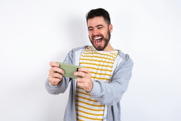 Portrait of an excited caucasian man wearing casual sportswear over white wall playing games on...