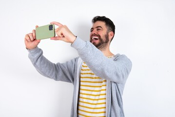 caucasian man wearing casual sportswear over white wall taking a selfie to post it on social media...