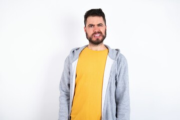 Portrait of dissatisfied caucasian man wearing casual sportswear over white wall smirks face,...