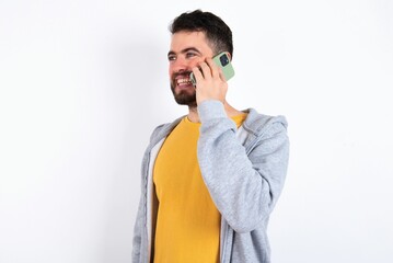 Happy joyful charming caucasian man wearing casual sportswear over white wall talk speak phone smile good mood