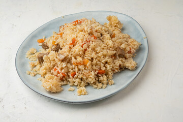 Rice with meat and vegetables in a plate, light background. Pilaf with meat.