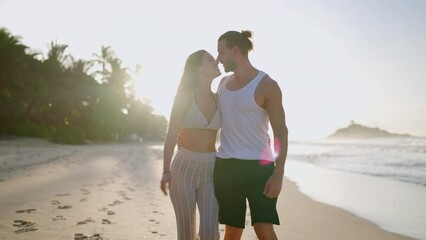 Young biracial happy couple and walking on the beach together enjoying summer front shot. Cheerful boyfriend and girlfriend relaxing and taking a walk at the seaside hugging and kissing at sunrise. - Powered by Adobe