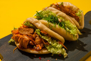 Bao buns three pieces on a wooden board, yellow background, hard light.