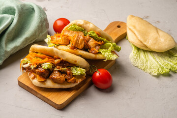 Asian-inspired bao buns on a wooden board and a gray background.
