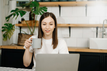 Confident beautiful Asian businesswoman typing laptop computer and digital tablet while holding coffee at home