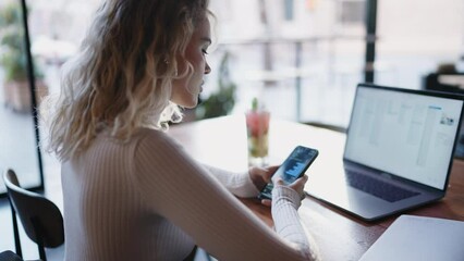 Female administrator using modern technology for remote work, managing tasks in smartphone application. Young woman freelancer typing text message on cellular while sitting at table in the coffee shop