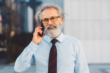 Portrait of senior businessman in light blue shirt with red tie talking on the phone outside smiling