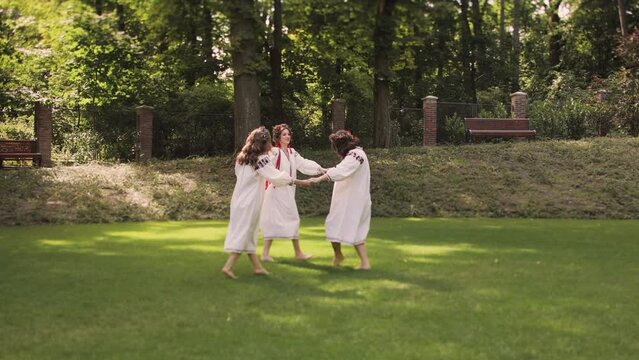 Three women in round dance roundelay. Girls wear Ancient ethno Ukrainian embroidered shirt dress and a wreath of flowers. Full shot