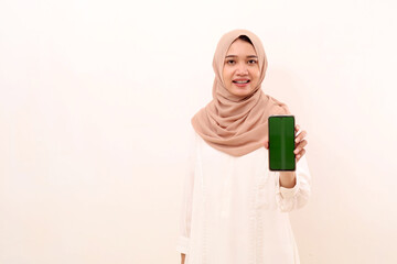 Happy young asian muslim woman showing blank cell phone display. Isolated on white with copyspace