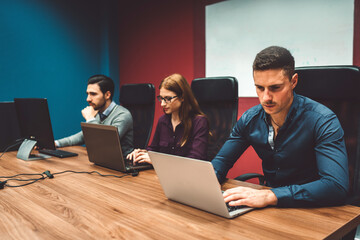 Colleagues at a start up company working on their laptops in colorful red and blue walls in the office 