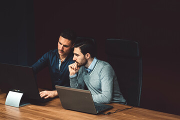 Two business man working in a dark room, on laptop and computer, thinking about ideas for a new...