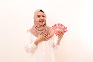 Happy relieved young asian muslim woman carrying indonesia banknotes while holding her chest