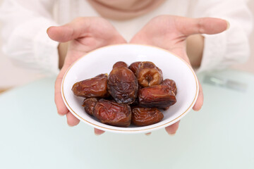 Young asian muslim woman's hand holding a plate of date palm fruit. Ramadhan concept.