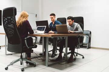 Group of three young business people working at a start up company, working together in the same office, each on his own laptop 