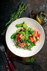 Green salad with fresh cucumbers, tomatoes, onions, basil, green leaves and crackers on a dark background. Healthy vegan food. Top view