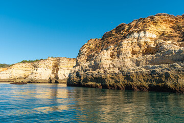 Fototapeta premium Natural caves and beach, Algarve Portugal. Rock cliff arches and turquoise sea water on coast of Portugal in Algarve region. View from the sea
