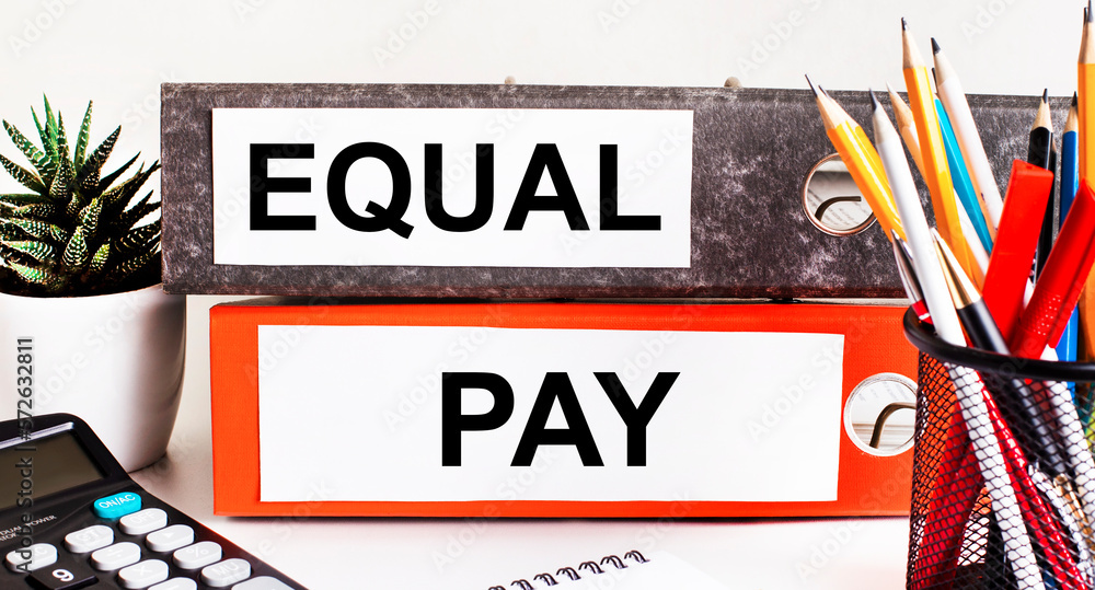 Poster on the desktop there are two folders for papers with the text equal pay, a calculator, pencils and a