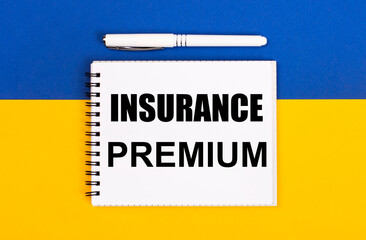 Obraz premium A white notebook with the text INSURANCE PREMIUM and a white pen on a blue and yellow background.