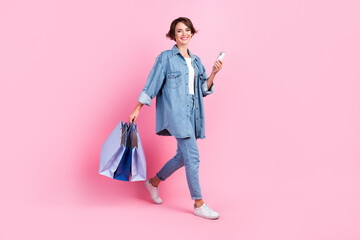 Full length photo of charming pretty lady dressed denim jacket holding bargains texting gadget isolated pink color background