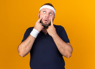 sad adult slavic sporty man wearing headband and wristbands pulling down eyelids with fingers...