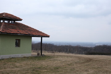 Green hunting lodge on the mountain, landscape in winter time, cloudy weather, dry grass, trees in the distance