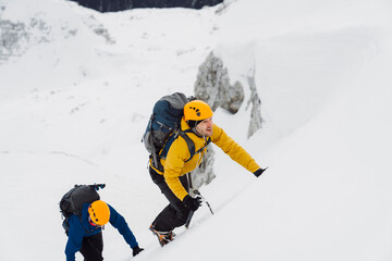 Mountaineer in yellow jacket leading the way for those bellow, climbing up a snowy mountain 