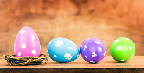 One Easter egg in a nest and three eggs on wooden table with defocused background. Easter concept